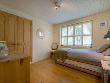 A bedroom with a single bed a wooden dresser a chair and a window with shutters at Grandpa Dickson's in Little Petherick