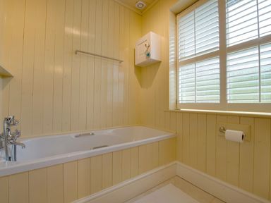 A bathroom with a bathtub metal towel rack window with shutters and a toilet paper holder at Grandpa Dicksons in Little Petherick