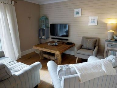 A living room with a wooden coffee table two armchairs a wall-mounted TV and a side table with a lamp at Grandpa Dickson's in Little Petherick
