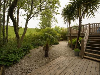 A garden area with gravel pathway wooden decking with stairs and trees at Grandpa Dicksons in Little Petherick