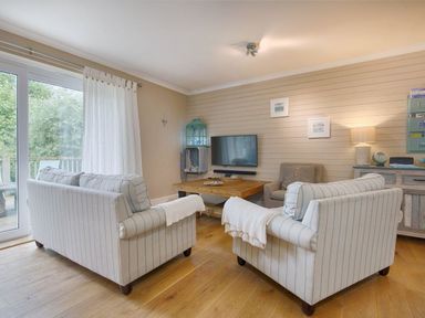 A living room with striped sofas a wooden coffee table and a wall-mounted television at Grandpa Dicksons in Little Petherick