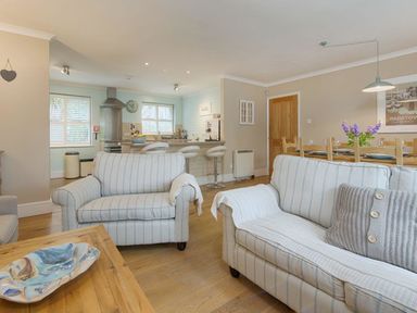 A living room with striped sofas a wooden table and an open kitchen and dining area at Grandpa Dickson's in Little Petherick