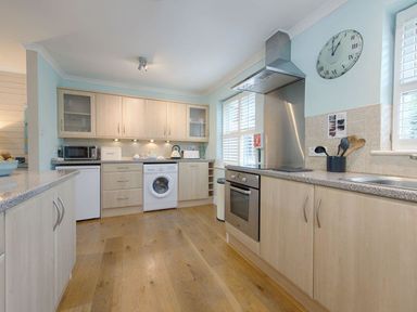 A kitchen with wooden cabinets and countertops a washing machine an oven a microwave and a clock on the wall at Grandpa Dickson's in Little Petherick