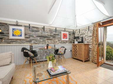 A seating area with two black chairs and a small glass table against a stone wall with framed pictures at Swallow Barn in St Kew