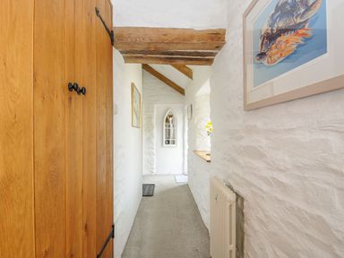 A narrow hallway with wooden door beams and white textured walls at Swallow Barn in St Kew