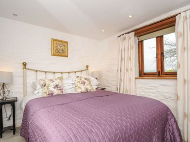 A bedroom with a bed covered by a purple quilt and floral pillows at Swallow Barn in St Kew