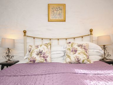 A bed with a metal headboard purple quilt floral pillows and two bedside lamps at Swallow Barn in St Kew