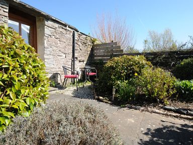 A small outdoor garden area with two chairs and a table next to a stone wall at Swallow Barn in St Kew