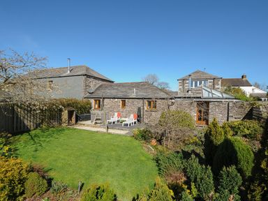 A backyard garden with grass lawn and plants in front of a stone house with sun loungers at Swallow Barn in St Kew