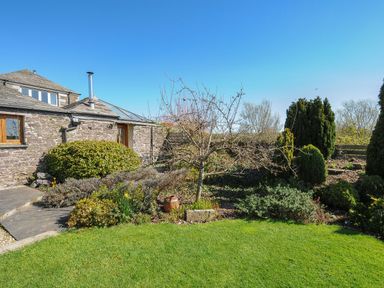 A garden with a small tree shrubs and green grass in front of a stone house at Swallow Barn in St Kew