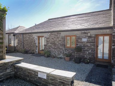 An exterior view of a stone building with two wooden doors and a window surrounded by gravel and potted plants at Swallow Barn in St Kew