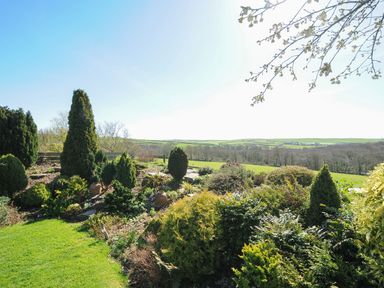 A garden area with shrubs and trees overlooking fields at Swallow Barn in St Kew