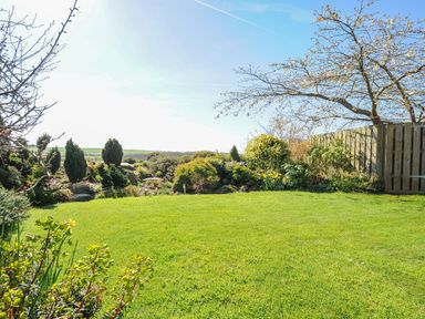 A garden with grass lawn trees shrubs and a wooden fence at Swallow Barn in St Kew