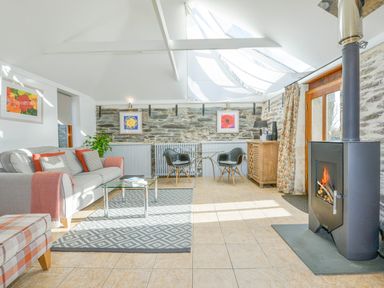 A sitting area with a sofa and two black chairs near a glass table and a wood burning stove at Swallow Barn in St Kew