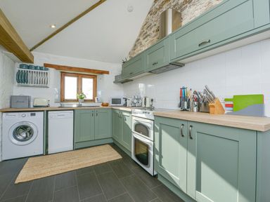 A kitchen with green cabinets a washing machine dishwasher oven and kitchen utensils at Swallow Barn in St Kew