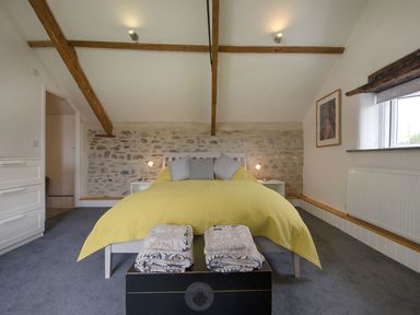 A bedroom with a yellow bedspread and folded blankets at the foot of the bed at Salty Cottage Morwenstow