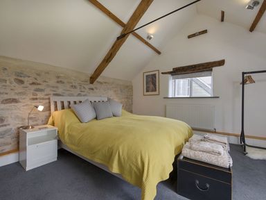 A bedroom with a bed covered with a yellow blanket next to a nightstand with a lamp and folded towels on a chest at Salty Cottage in Morwenstow