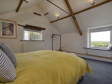 A bedroom with a yellow bedspread wooden beams and two windows with countryside view at Salty Cottage in Morwenstow