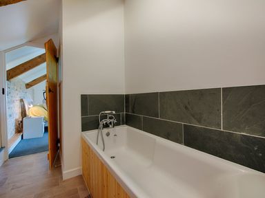 A bathroom with a bathtub and tiled wall next to a doorway leading to a bedroom at Salty Cottage in Morwenstow