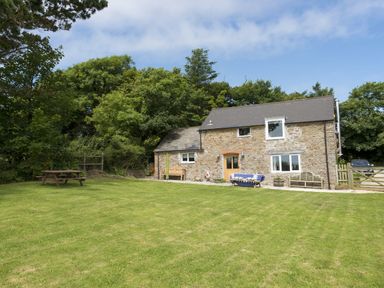 A stone house with a lawn and outdoor seating surrounded by trees at Salty Cottage in Morwenstow