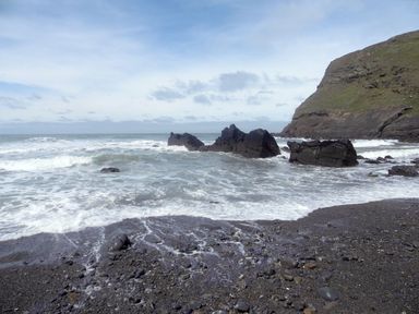 A rocky beach with waves crashing on shore and cliffs in the background at Salty Cottage in Morwenstow