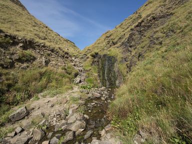 A small waterfall and rocky stream between grassy hills under a blue sky at Salty Cottage in Morwenstow