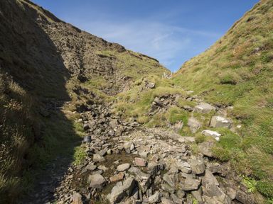A rocky path with grass-covered hills on both sides under a clear sky at Salty Cottage in Morwenstow