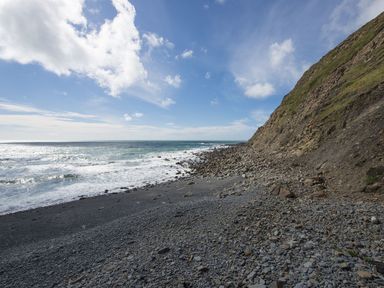 A rocky beach with waves and a steep cliff under a partly cloudy sky at Salty Cottage in Morwenstow