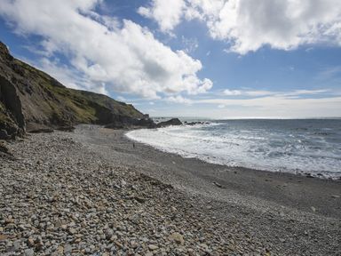 A rocky beach with waves and cliffs under a cloudy sky at Salty Cottage in Morwenstow
