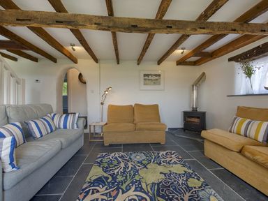 A living room with sofas rug wood burner and exposed ceiling beams at Salty Cottage in Morwenstow