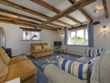 A living room with wooden-beamed ceiling sofas television and a patterned rug at Salty Cottage in Morwenstow