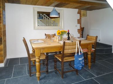 A dining room with a wooden table set for four and a blue pendant light above at Salty Cottage Morwenstow