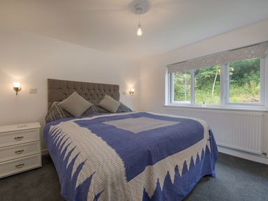 A bedroom with a bed covered in a blue and white patterned blanket next to a window at Salty Cottage in Morwenstow