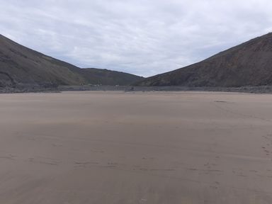 A sandy beach with hills on both sides and cloudy sky at Salty Cottage in Morwenstow