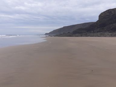 A sandy beach with waves and rocky cliffs under a cloudy sky at Salty Cottage in Morwenstow