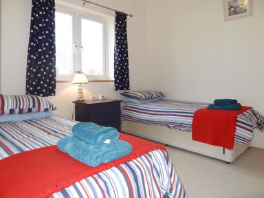 A bedroom with two single beds striped bedding red blankets and blue towels at The Loft in Bude