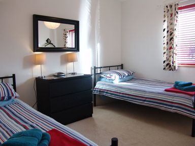 A bedroom with two single beds striped bedding and a black chest of drawers with two lamps at The Loft in Bude