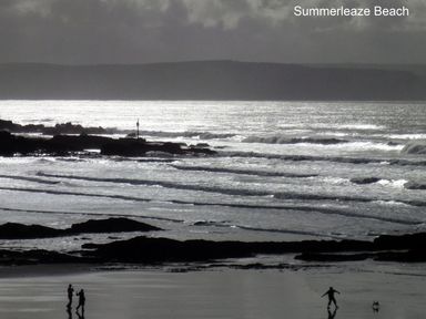 A beach with waves and rocks and people walking with a dog at Summerleaze Beach