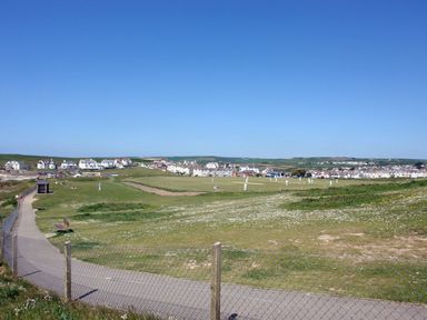 A sports field with players in white uniforms a fence and pathway in the foreground and houses in the background at The Loft in Bude