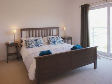 A bedroom with a wooden bed with white bedding and blue patterned pillows beside side tables with lamps and towels on the bed at The Loft in Bude