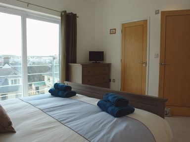 A bedroom with a bed holding folded towels a chest of drawers with a small TV and two wooden doors at The Loft in Bude