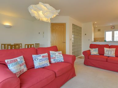 A living room with red sofas and decorative pillows with a wooden dining table behind at The Loft in Bude