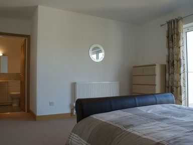 A bedroom with a bed a dresser a radiator a round mirror on the wall and an open door leading to a bathroom at Seagulls Perch in Mawgan Porth