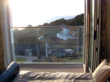 A bedroom with a bed and open glass doors leading to a balcony overlooking a hillside and ocean at Seagulls Perch in Mawgan Porth