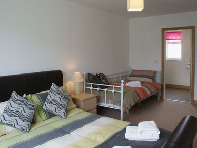 A bedroom with two beds a bedside table with a lamp and an open door showing a small room at Seagulls Perch in Mawgan Porth