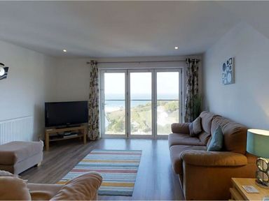 A living room with a sofa a television a striped rug and large glass doors with a view at Seagulls Perch in Mawgan Porth
