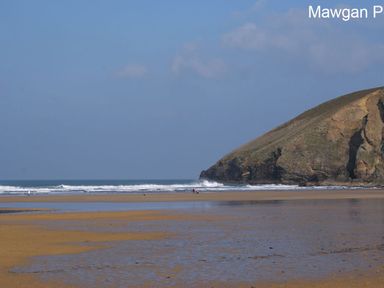 A sandy beach with small waves and a large rocky hill in the background at Seagulls Perch in Mawgan Porth