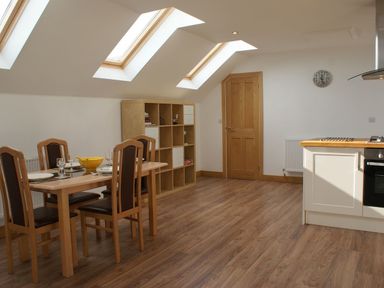 A dining area with a wooden table and four chairs next to a shelving unit under skylights at Seagulls Perch in Mawgan Porth