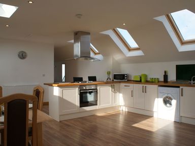 A kitchen with white cabinets wood countertops and skylights at Seagulls Perch in Mawgan Porth