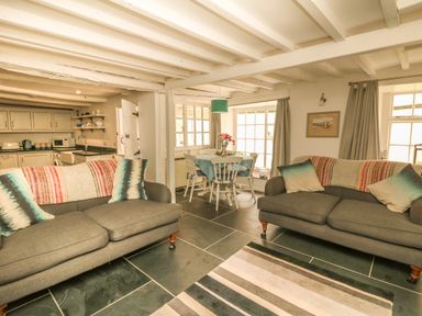 A living room with two grey sofas and a dining table with chairs near windows at Cousham Cottage in Kingsand And Cawsand